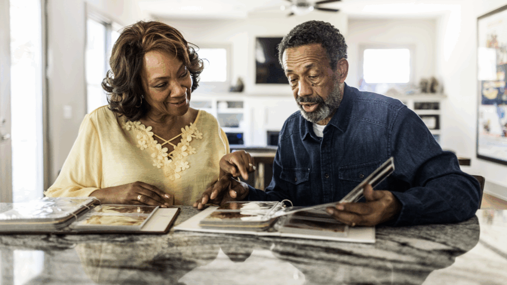 A senior woman and a senior man sip coffee while looking at old family photos